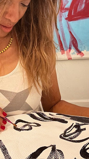 Woman painting black designs on a white surface with a brush.