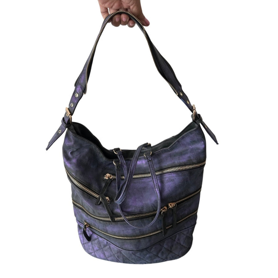 Purple handbag with gold zippers held by a hand on a white background