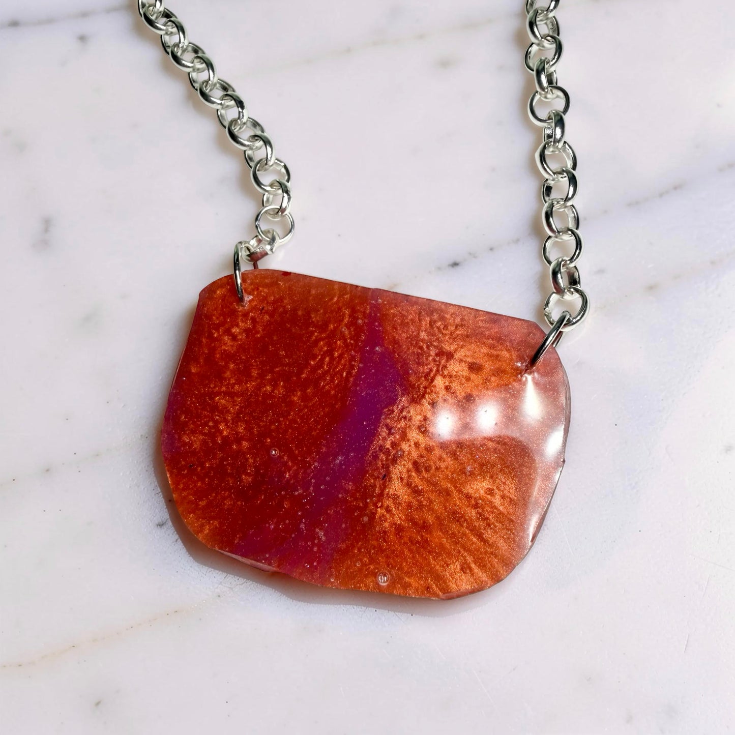 Necklace with a red-orange and purple pendant on a marble background
