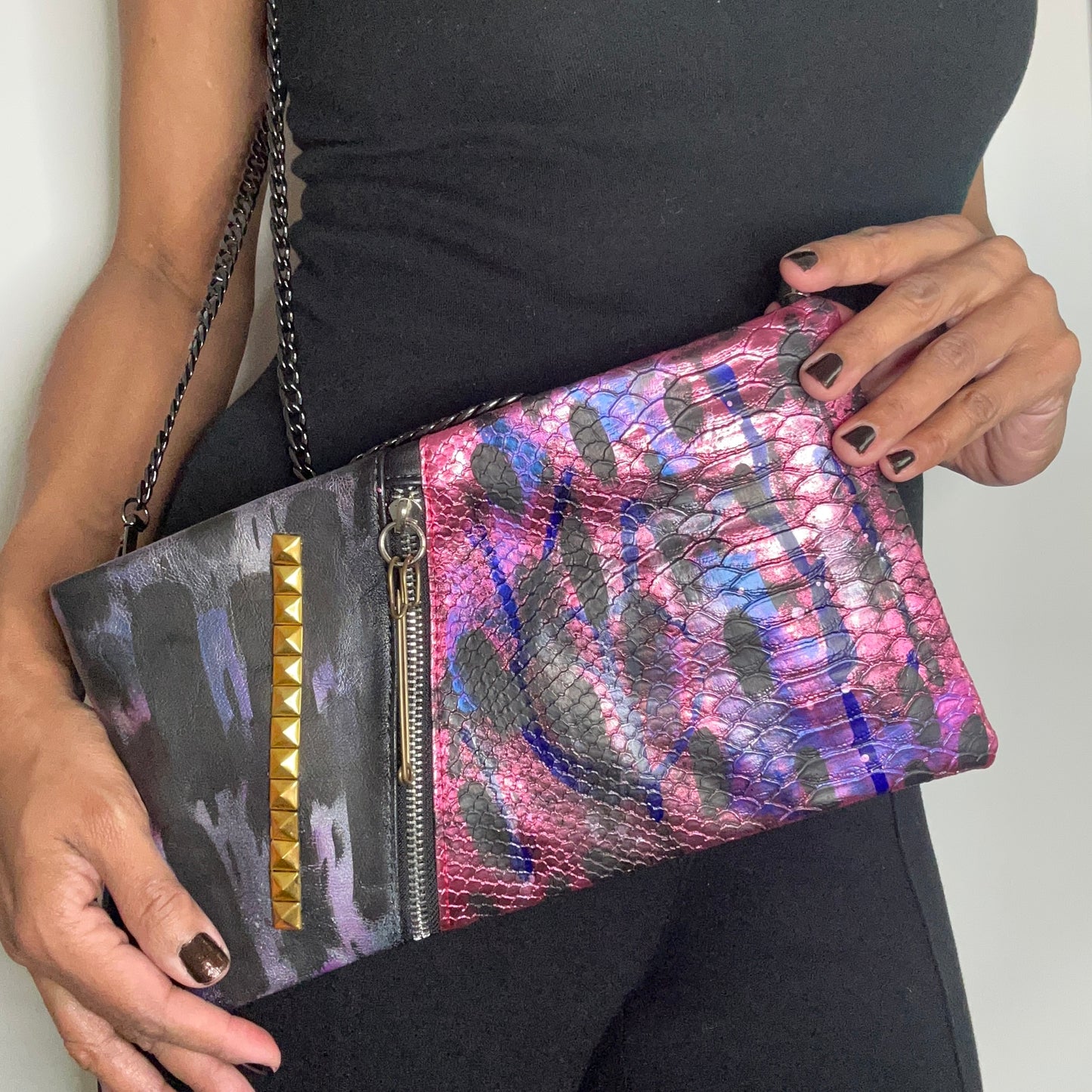 Multicolored clutch with studded detail held by a person wearing a black top.