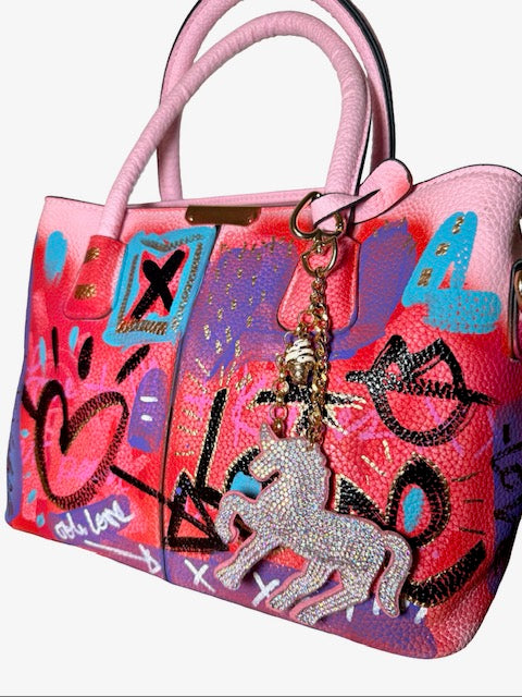 Colorful handbag with artistic designs and a unicorn charm on a white background