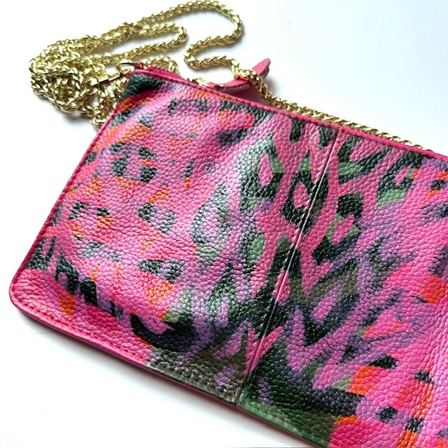 Pink clutch with floral pattern and gold chain strap on a white background