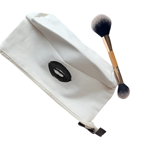 Makeup brush and black oval compact on a white pouch against a light gray background