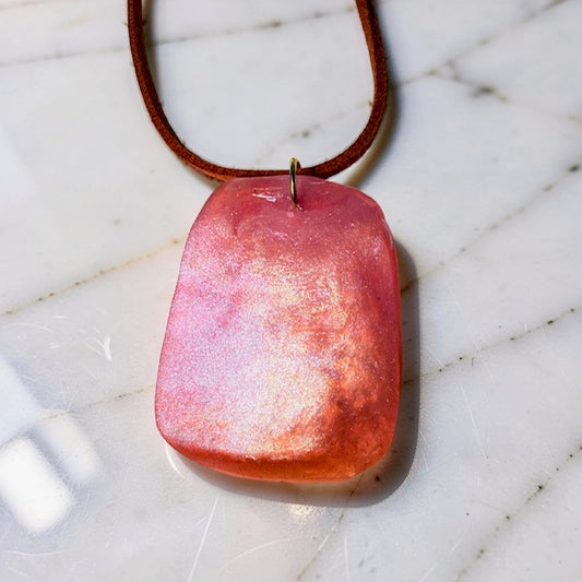 Orange pendant on a brown cord against a white tiled background