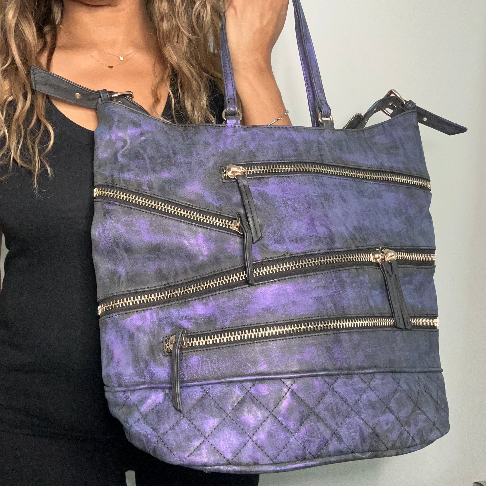 Purple handbag with gold zippers held by a person against a neutral background