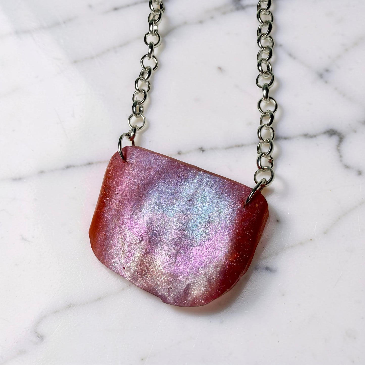 Necklace with a pink and purple pendant on a marble background