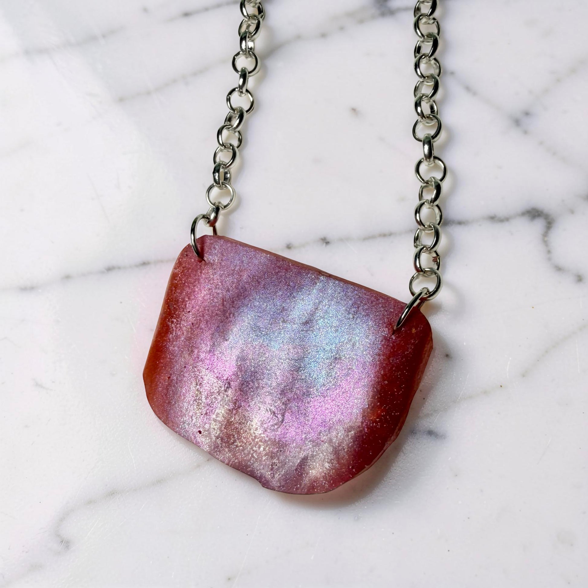 Necklace with a pink and purple pendant on a marble background