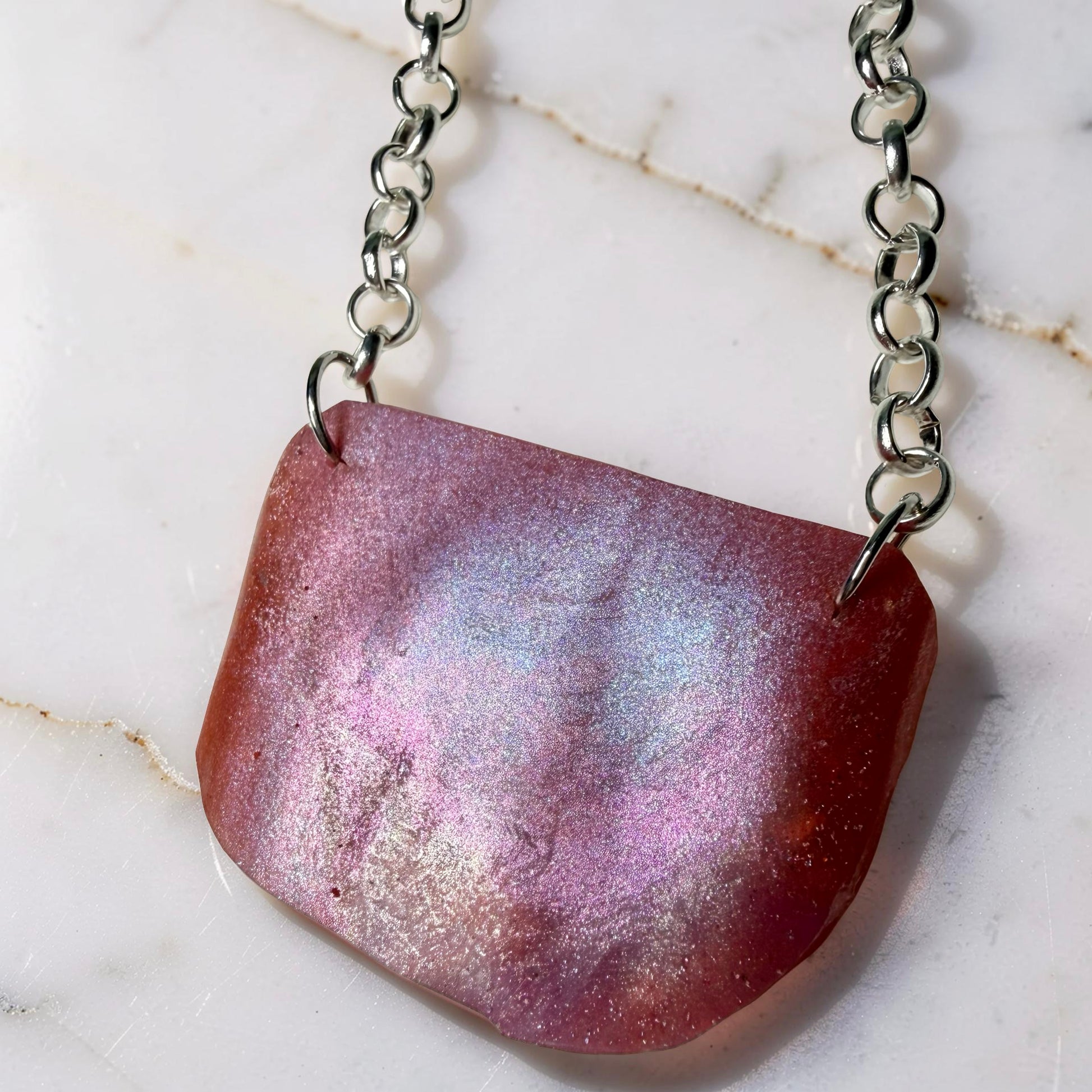 Necklace with a pink and purple pendant on a marble surface
