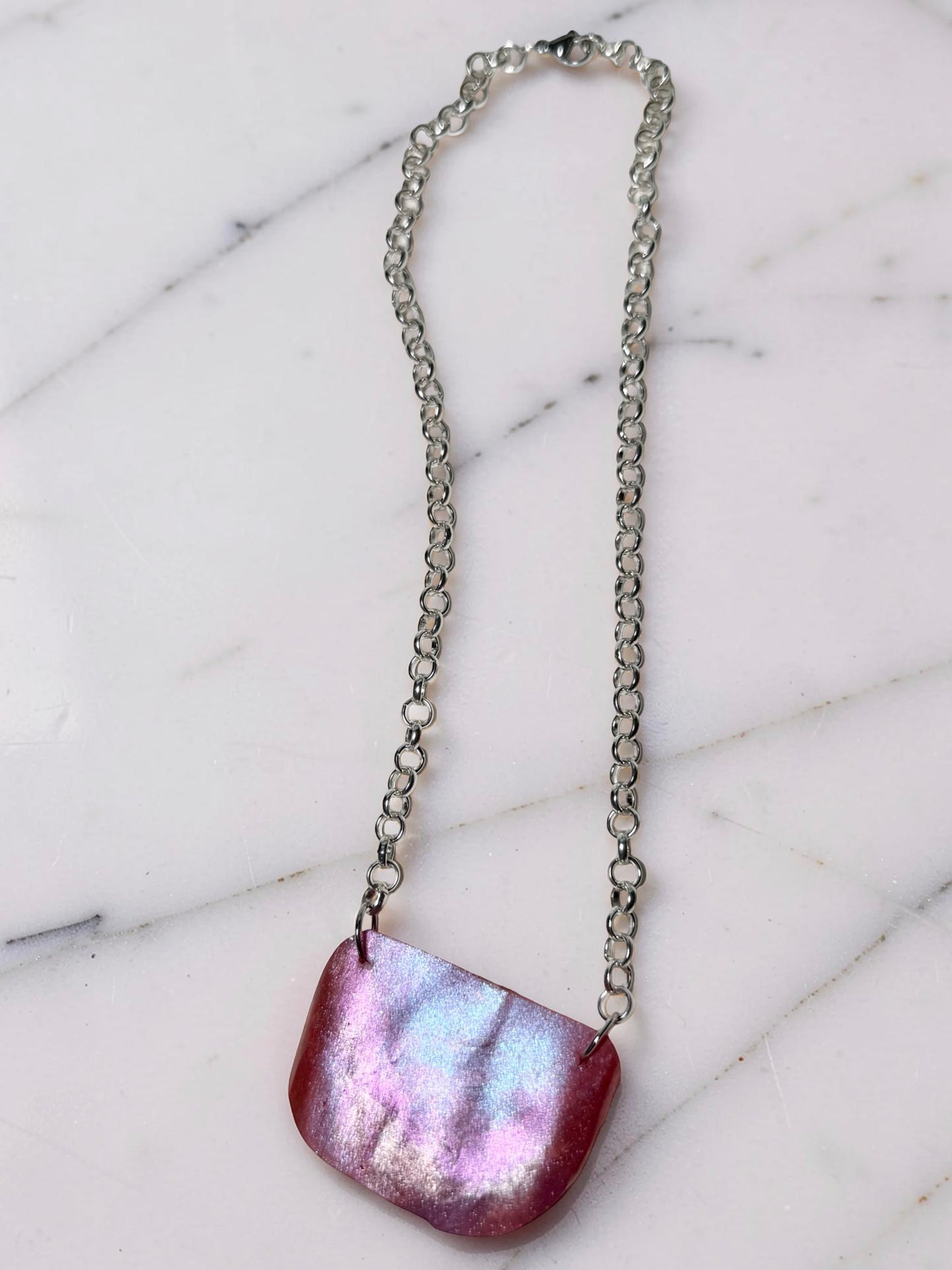 Necklace with a pink, iridescent pendant on a marble surface