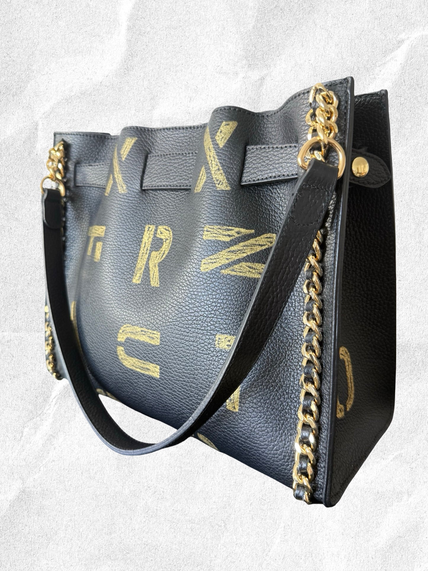 Edgy Black handbag with gold chain detail and decorative lettering on a light gray background