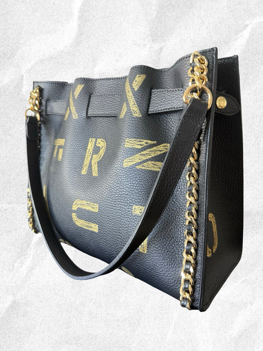 Edgy Black handbag with gold chain detail and decorative lettering on a light gray background