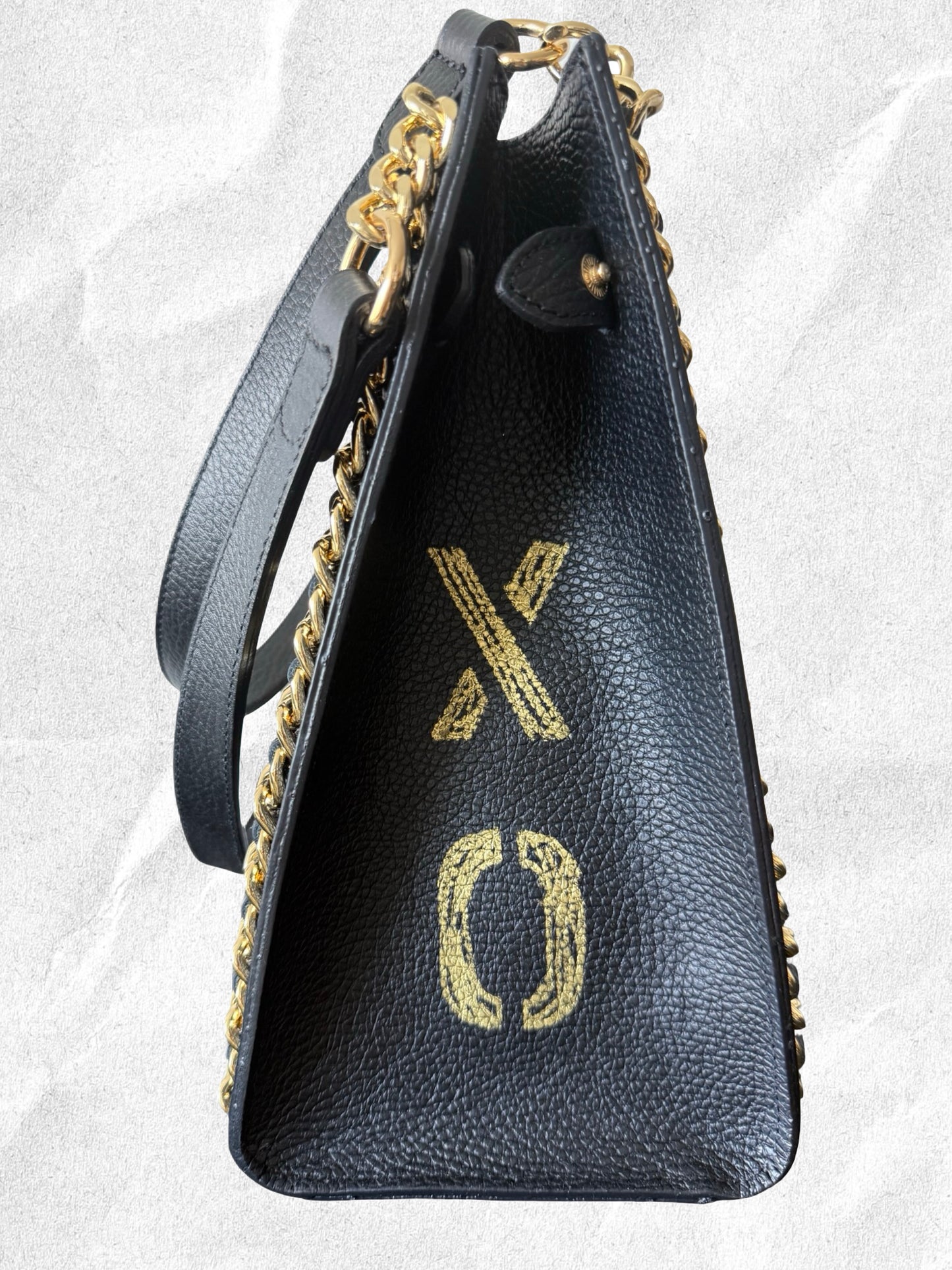Black handbag with gold chain strap and 'xo' logo on a light gray background