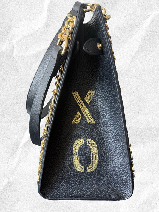 Black handbag with gold chain strap and 'xo' logo on a light gray background