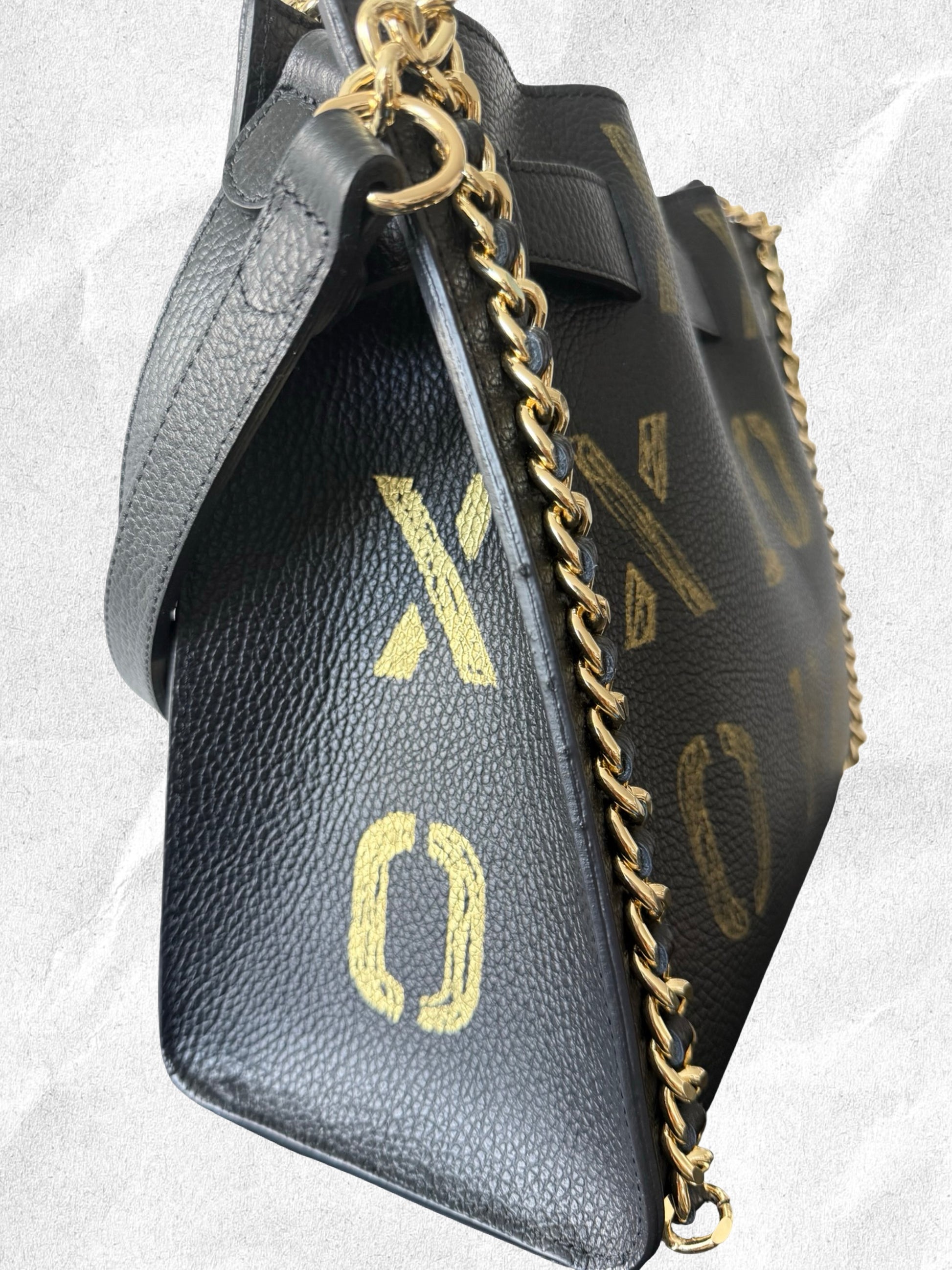 Black handbag with gold chain strap on a light gray background