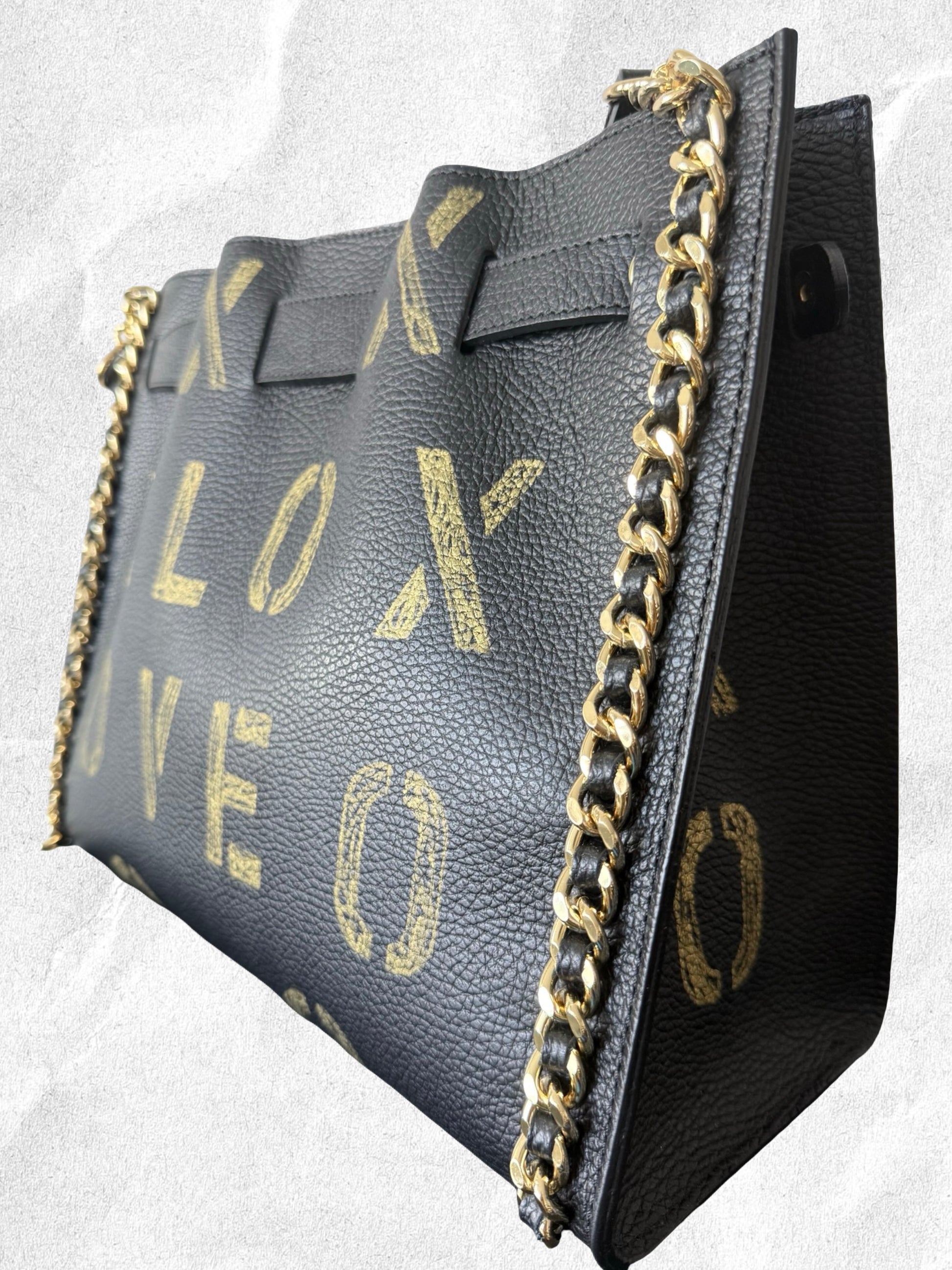 Black handbag with gold chain strap and gold lettering on a light gray background