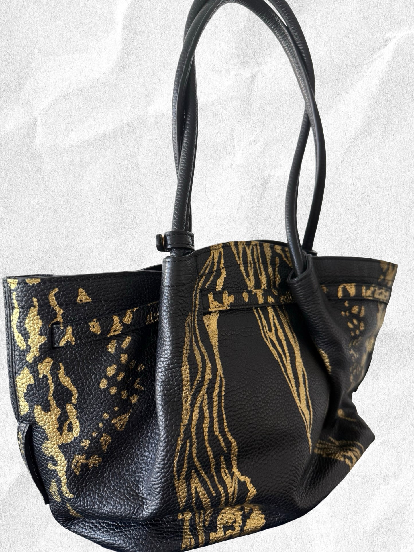 Black leather handbag with gold abstract pattern on a light gray background