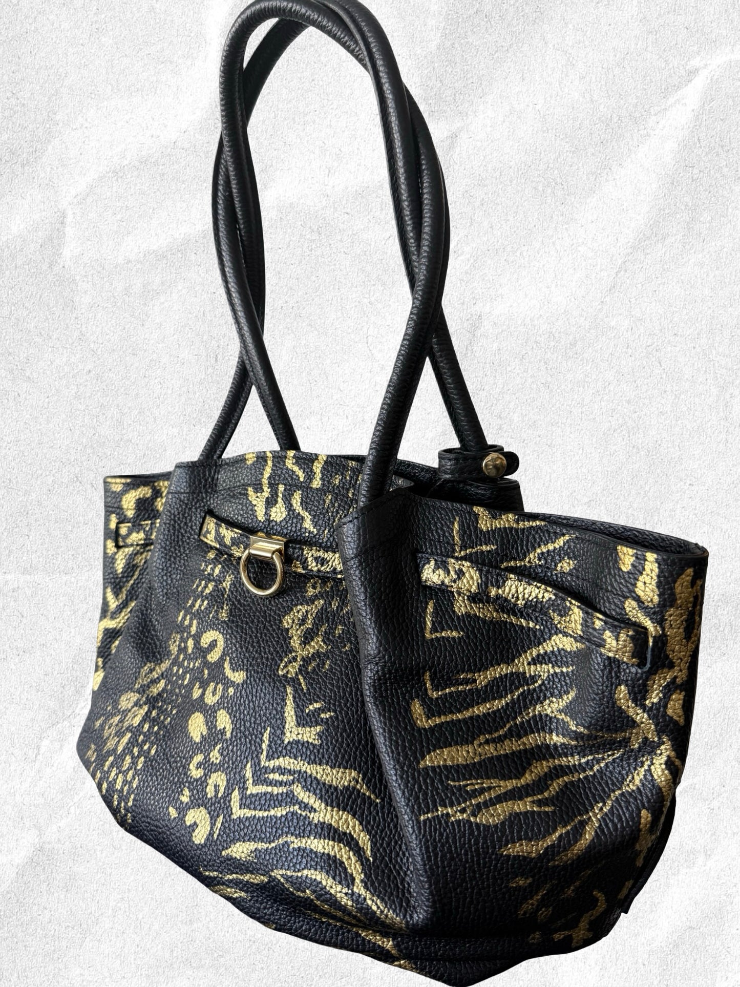 Black handbag with gold zebra print on a textured white background