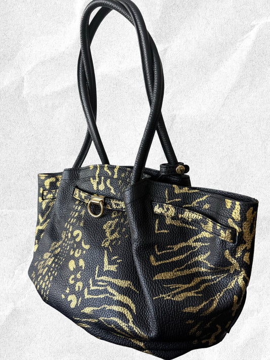 Black handbag with gold zebra print on a textured white background