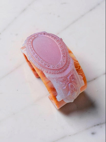 Decorative classical design bracelet with pink top and orange bottom on a white marbel surface