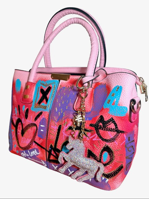 Colorful handbag with graffiti-style design and unicorn charm on a white background