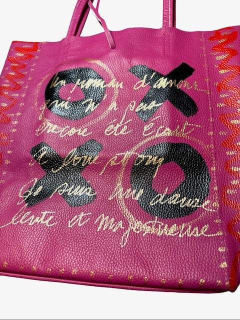 Pink leather tote bag with black and gold text and designs on a white background