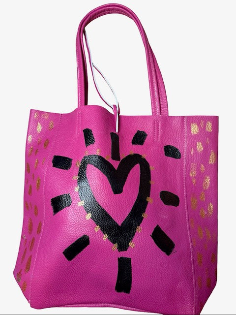 Pink leather tote bag with black heart design and gold accents on a white background