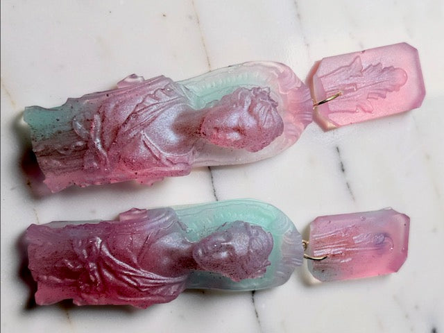 Pair of translucent earrings shaped like classical figures on a marble surface