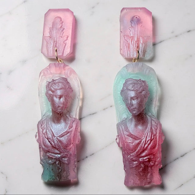 Pair of goddess statue pink and aqua blue earrings on a marble surface