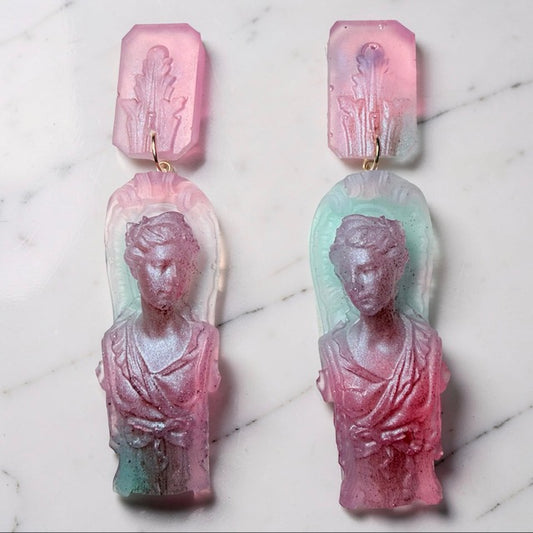 Pair of goddess statue pink and aqua blue earrings on a marble surface