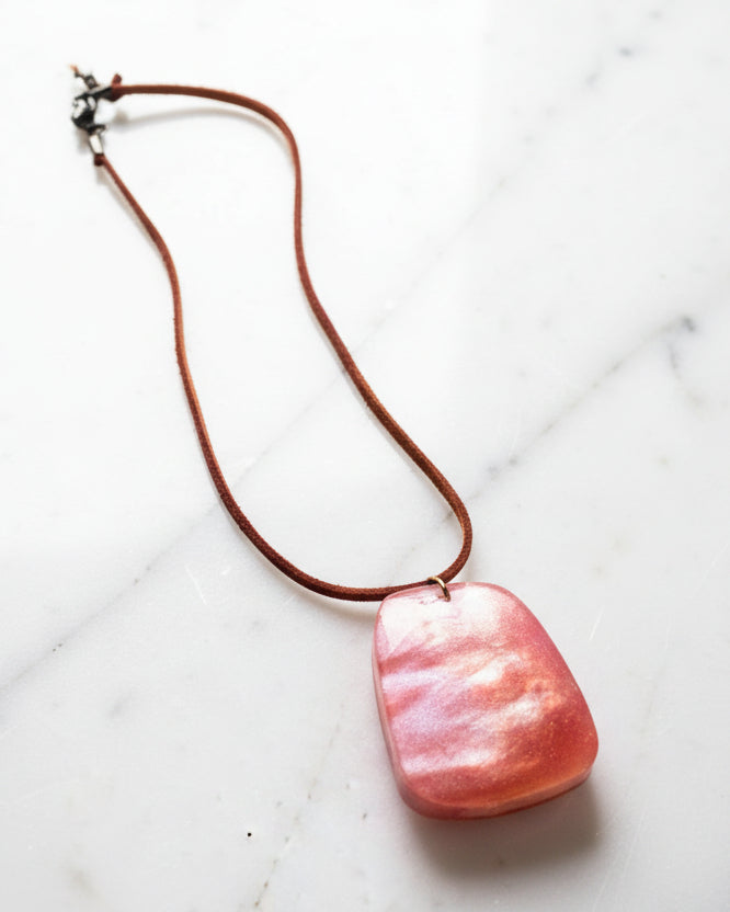 Necklace with a dark iridescent orange pendant on a marble surface