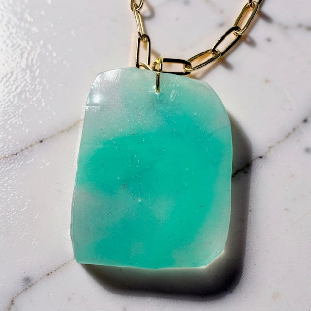 Turquoise pendant on a gold chain against a marble background