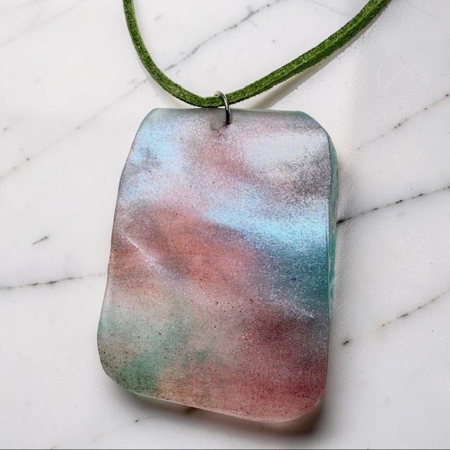 Multicolored pendant on a green cord against a marble background