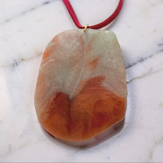 Marbled stone pendant on a red cord against a marble background