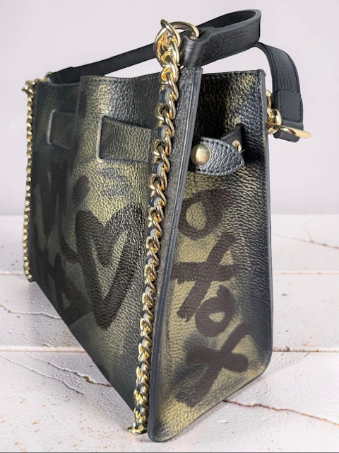 Handbag with graffiti pattern and gold chain detail on a light wooden surface